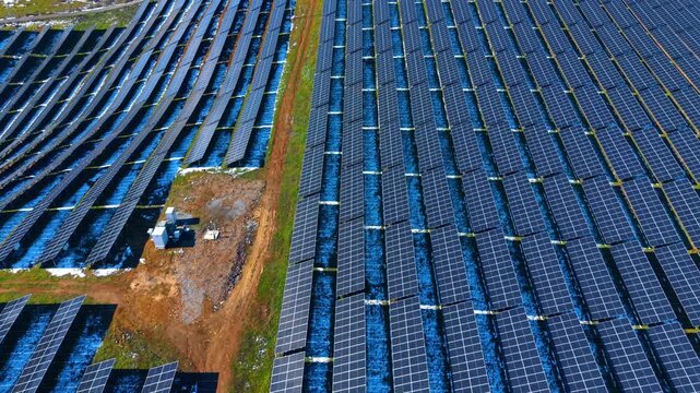 Aerial view of solar farm with transformer station. Drone shot of solar panel rows and electrical infrastructure on the ground in a rural area.