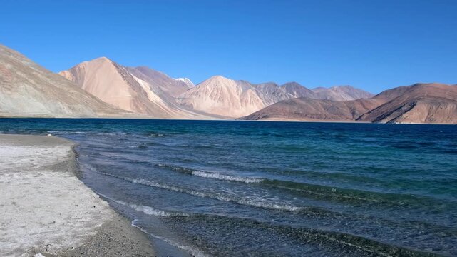 Cinematic shot of Pangong Lake during early morning, with soft golden light reflecting on the calm water as birds gently glide across the surface. Ideal moment for travel and nature storytelling.