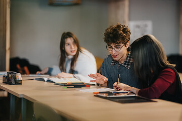 Fototapeta premium Three students study and discuss papers and notes at a long table. A small study group collaborates and shares ideas while working on assignments.