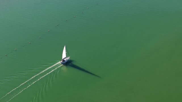 Aerial view of a lone sailboat gracefully sailing through the vivid green waters, leaving a trail in its wake, Ipswich, England, United Kingdom.