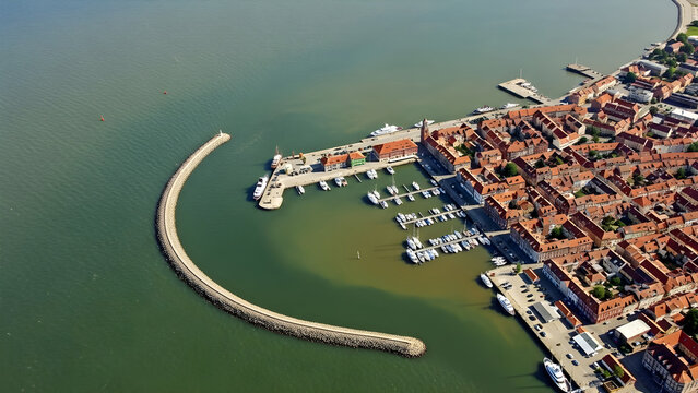 Aerial view of a coastal town with a curved breakwater and boats docked in the harbor near buildings