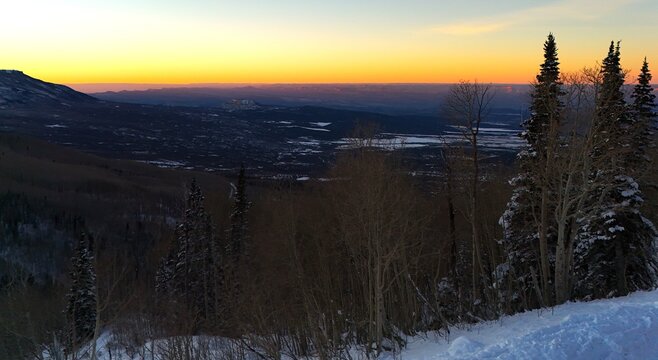 Aerial view of a landscape bathed in the warm glow of the setting sun, casting long shadows across the snow-dusted terrain, Grand Mesa, Colorado, United States.