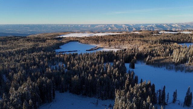 Aerial view of a landscape bathed in the warm glow of the setting sun, casting long shadows across the snow-dusted terrain, Grand Mesa, Colorado, United States.