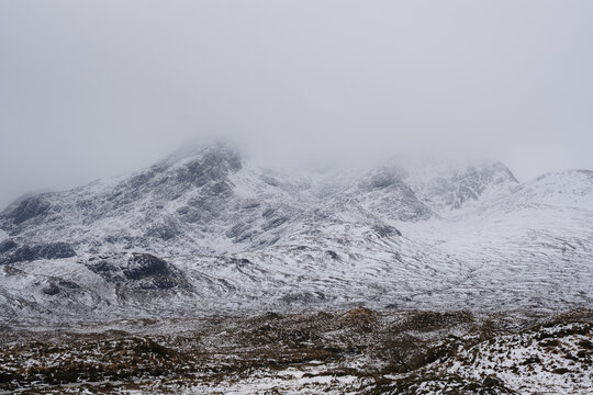 View of snow-covered Cuillin mountains rise majestically, shrouded in mist and cloud, creating a serene yet powerful landscape, Isle of Skye, Scotland.
