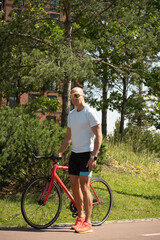 Naklejka premium Athletic man standing with bicycle in park
