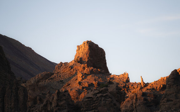 View of golden sunlight bathing the rugged rock formations of Roques de Garcia, casting long shadows and highlighting the textures of the landscape, Teide National Park, Tenerife, Spain.