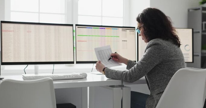 Analyst woman reviewing spreadsheets on office computer. She audits data across monitors, validating figures and reports for finance decisions. Concept highlights financial analysis accuracy.