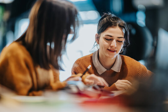 Two young women study together, sharing notes and focusing on their work. The pair collaborate and discuss ideas in a relaxed, indoor study session.