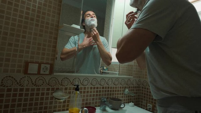 Man Shaving Face in Bathroom Mirror During Morning Routine
