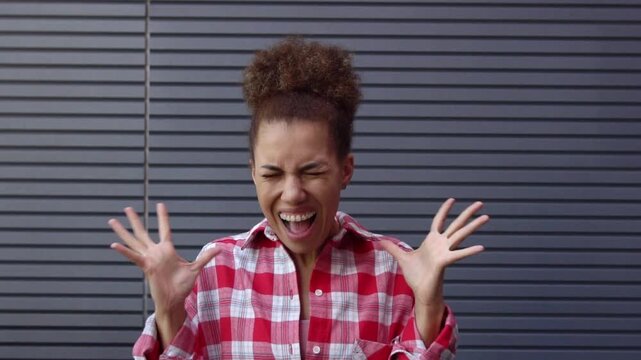 African American woman screaming hysterically against urban wall, angry girl stressed outdoors