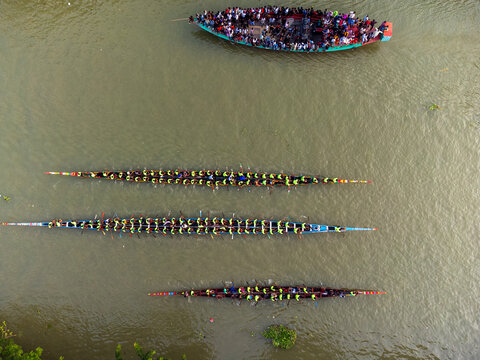 Aerial view of vibrant dragon boats cutting through the murky waters, complemented by a spectator-filled boat, Gopalganj, Dhaka Division, Bangladesh.