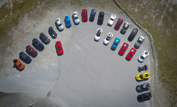 Bonneval-sur-Arc, France - 28 September 2019: Aerial view of a vibrant array of colorful cars elegantly arranged in a semi-circle on a vast, textured gray surface, like jewels scattered on stone..
