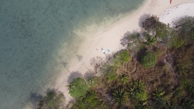 Vertical aerial drone footage capturing the pristine coastline of Ko Man Nai near Koh Chang, Thailand. Turquoise water, untouched sandy beaches and dense tropical jungle.