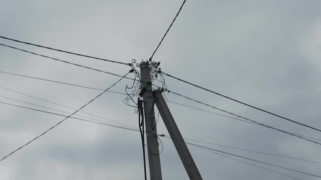 Electric pole with tangle of wires against a cloudy gray sky. Infrastructure and energy transmission system. Network of cables providing electrical power to urban or rural environments.