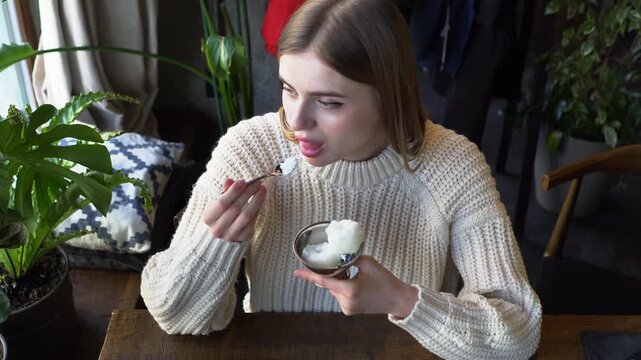 young beautiful woman eats ice cream with spoon in cafe, girl eats plombir dessert in restaurant