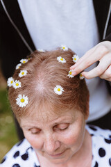 A girl puts daisies in a woman's hair in a park.