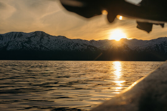 View of golden sunset bathes the tranquil waters as jagged, snow-capped mountains loom in the background, casting long shadows over the serene landscape, Husavik, Iceland.