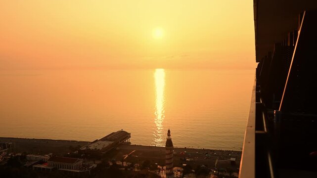 Sunset over Black Sea in Batumi, Georgia. Aerial View from Balcony of Orbi City. Golden Hour Sunlight Reflecting on Water. Cityscape with Alphabet Tower and Pier. Summer Vacation Travel Concept.