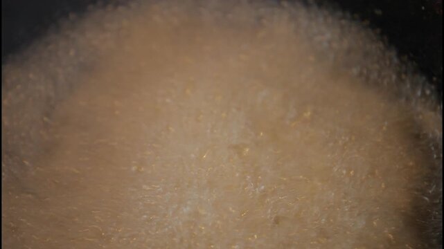 Deep frying traditional Turkish handmade dough nuggets in hot oil, close-up shot with a slight zoom-in as bubbles form, Mediterranean street food preparation.