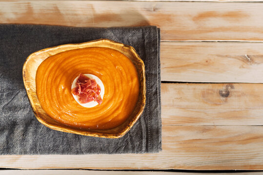 Rustic plate with salmorejo accompanied by boiled egg and ham, on a rustic white wooden table.