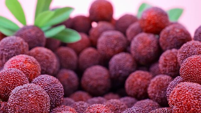 Extreme Macro Close-up of Fresh Red Yangmei Chinese Bayberry Pile with Green Leaves on Pink Background, Food Ads