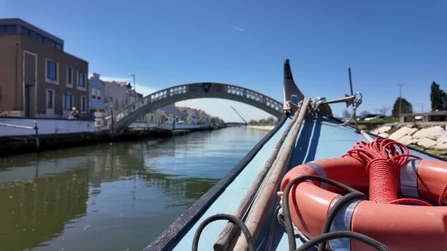 Traditional moliceiro boat sailing through a canal under a bridge in Aveiro, Portugal