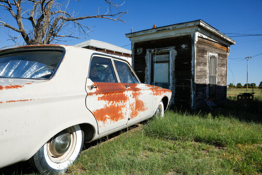 Rusted vintage car beside abandoned cabin