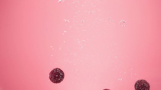 Slow Motion Macro of Fresh Red Yangmei Chinese Bayberry Falling into Water with Bubbles and Splashes on Pink Background