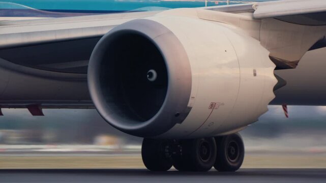 Close up view of a commercial airplane jet engine turbine spinning and landing gear wheels rolling on the airport runway. The aircraft is accelerating for takeoff or taxiing on the tarmac