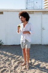 Multiethnic man smiling while enjoying a refreshing drink on a sandy beach