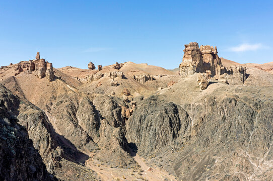 Panoramic view of the multi-colored sedimentary layers and towering rock pillars crowning the rugged mountainsides of Charyn Canyon in Kazakhstan