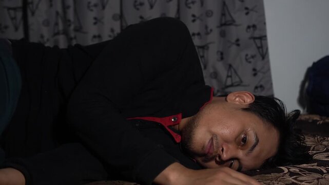 A thoughtful Southeast Asian man lying awake in bed at night, staring blankly with a sad expression. Themes of insomnia, depression, mental health struggle, loneliness, and contemplation in a dark bed