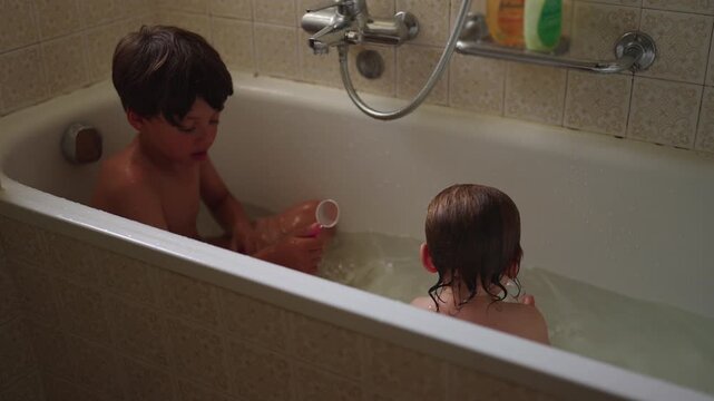 Two children sitting together in bathtub playing with water and objects joyful sibling interaction during bath time routine playful moment of bonding and shared activity