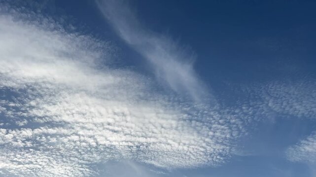 Time-lapse of beautiful white altocumulus clouds moving across the bright blue sky