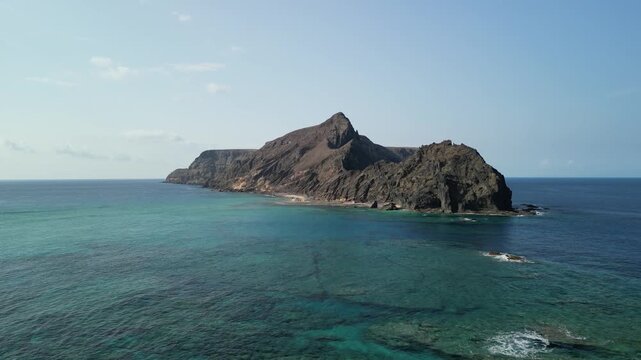 Aerial view of drone flying over Ilheu da Cal, a small rock island in Porto Santo, Madeira, Portugal. Portuguese paradise with clean transparent water.