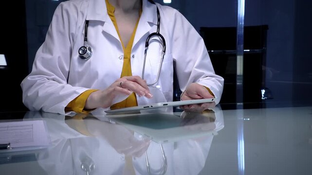 Female doctor wearing a white lab coat and stethoscope, using a digital tablet for telemedicine consultation, reviewing patient records, or managing hospital information system