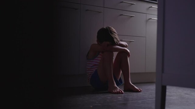 Young boy sitting alone on kitchen floor hugging knees while crying softly, emotional childhood moment expressing loneliness vulnerability and inner distress