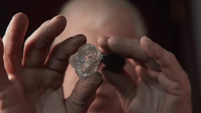 Jeweler examining large rough diamond up close in workshop.