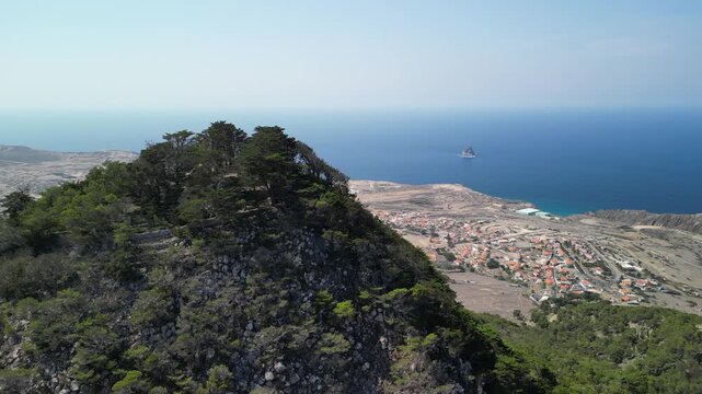 Aerial view of drone flying around Pico do Castelo mountain, with a shape of a vulcano. Porto Santo Island, Madeira, Portugal. Airport and long beach in the background