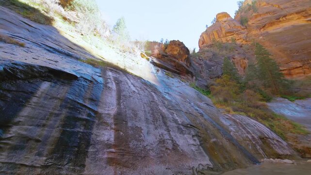 Footage of a hiker near Mystery Falls, a 120-foot waterfall flowing into the Virgin River within Zion National Park's iconic Narrows slot canyon in Utah. The Narrows is a world-famous hike through dra