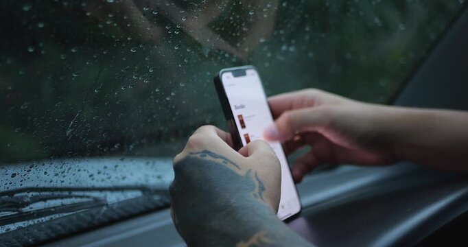 Tattooed Hands Using Smartphone Inside Car During Rain, Wet Window And Blurred Background, Mobile Browsing, Travel Pause, Moody Weather And Technology Concept