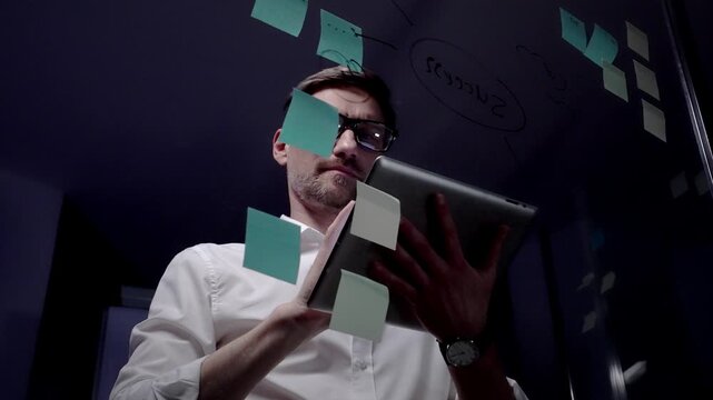 Man in eyeglasses organizing thoughts and ideas for business optimization on a clear glass board. Creating a strategic roadmap for innovation and project planning
