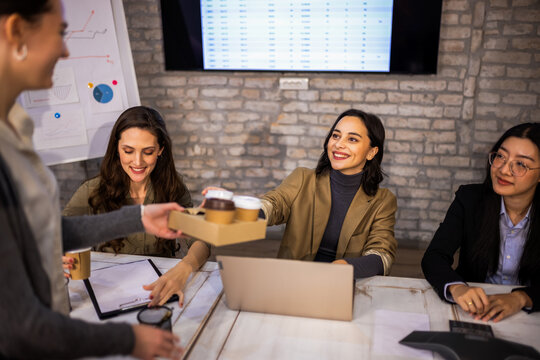 Kind female colleague bringing coffee to coworkers working at their desks in a modern office.