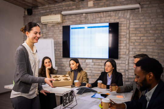 Diverse colleagues receiving coffee from a coworker while working on laptops in a corporate office.