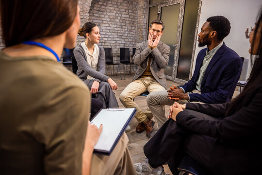 Diverse office workers sitting in a circle for a group mental health session with a professional therapist.
