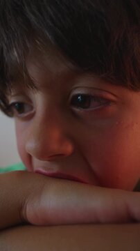 Extreme close up of child face resting on arm while looking ahead at off camera screen capturing immersive attention subtle emotion and digital engagement