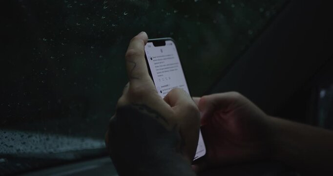 Tattooed Hands Scrolling Smartphone Feed Inside Car During Rain. Wet Window And Dark Moody Atmosphere. Social Media Browsing. Reading News