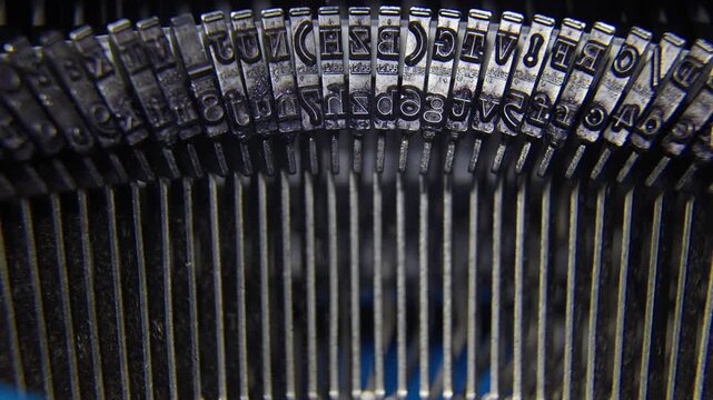Extreme close-up of mechanical metal hammers and letters of an old typewriter moving while typing.