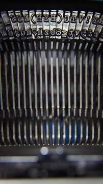 A vertical close-up shot of an antique typewriter mechanism showing metal typebars striking in a rhythmic motion.