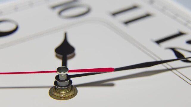 A macro shot of a white clock face showing the red second hand and black minute hand in motion.